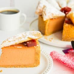 Preview image: A slice of Pastelillo de Guayaba Cheesecake on a white plate in front of a mug of coffee and the rest of the cheesecake.
