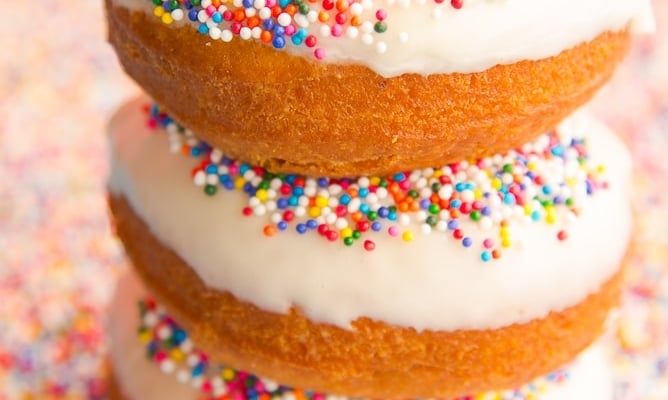 Lead image of a stack of 3 Tres Leches Cake Donuts in a bed of rainbow sprinkles.