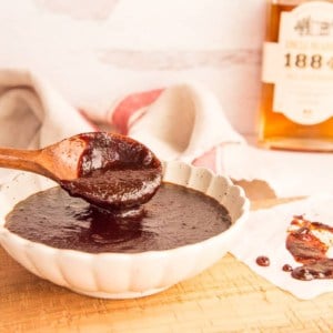 Preview image: a spoon lifts Uncle Nearest BBQ Sauce from a beige bowl which is on a wooden surface.