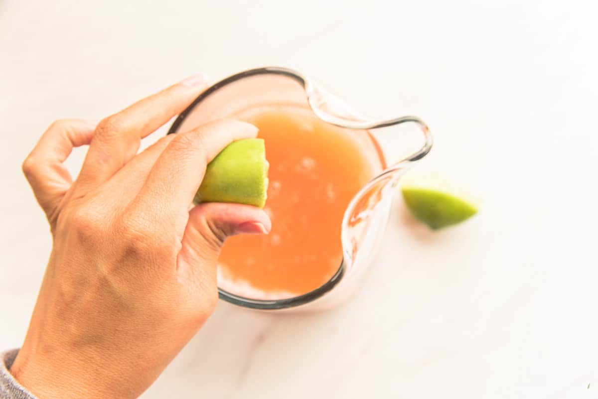 Fresh lime juice is squeezed from a half of lime into the pitcher of liquors