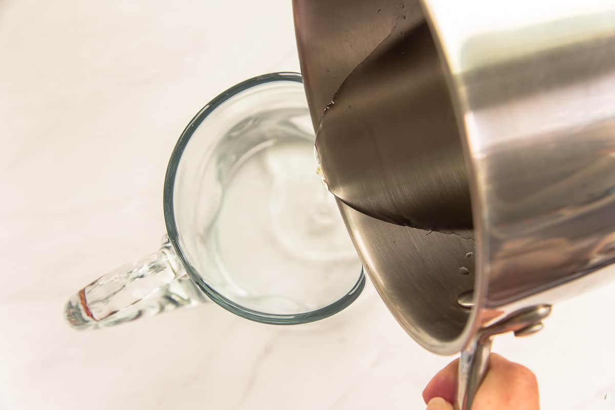 Simple syrup is poured from a silver pot into a clear glass pitcher