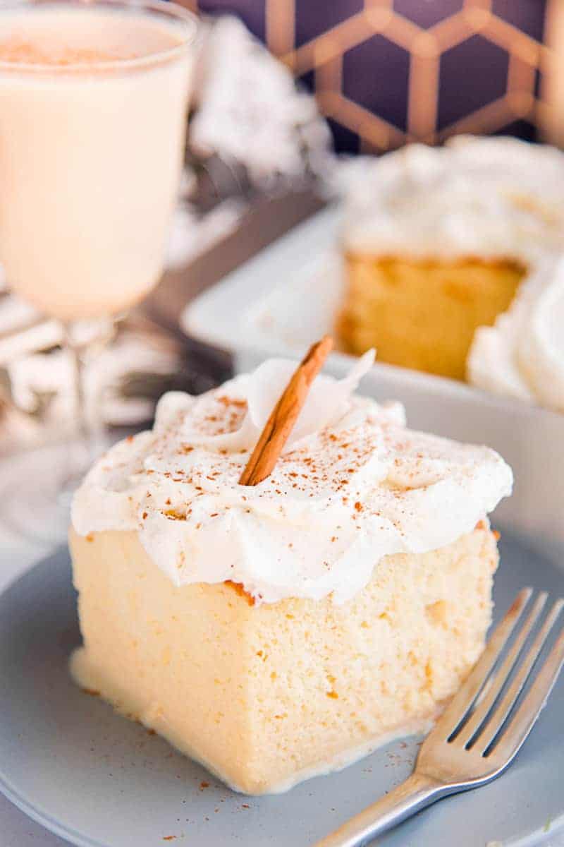 A slice of coquito tres leches on a light blue plate garnished with a cinnamon stick. 