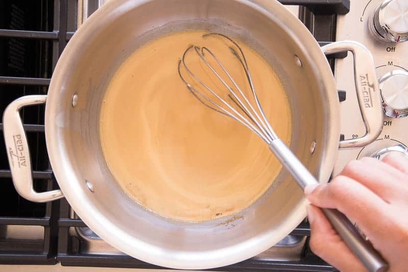 A whisk is used to stir the ingredients for the amaretto cream sauce together in a silver pot