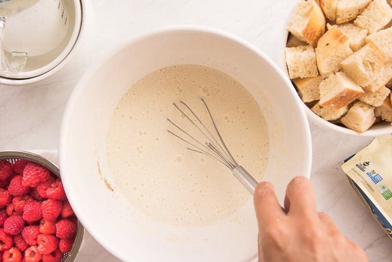 The ingredients for the bread pudding custard are whisked together in a white ceramic bowl
