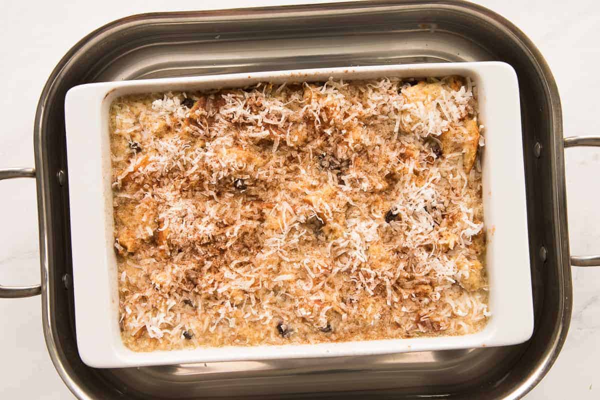 The Coquito Bread pudding in a white baking dish is uncovered to finish baking and browning.