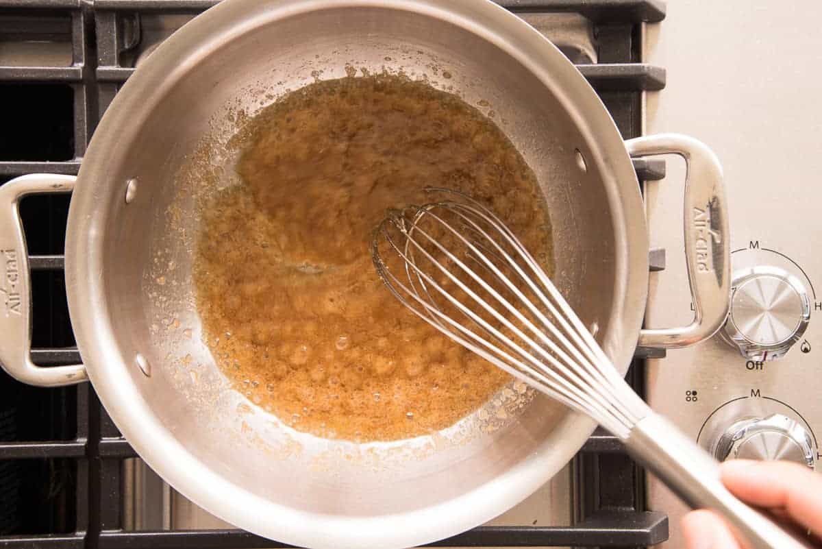 The brown sugar is whisked into the melted butter in a silver pot.