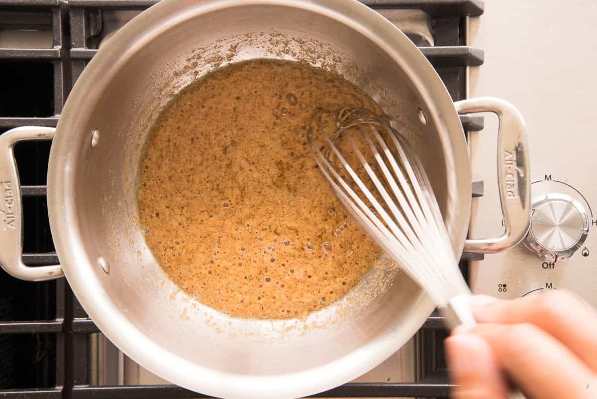 The butter in the pot separates from the brown sugar as a whisk stirs the two.