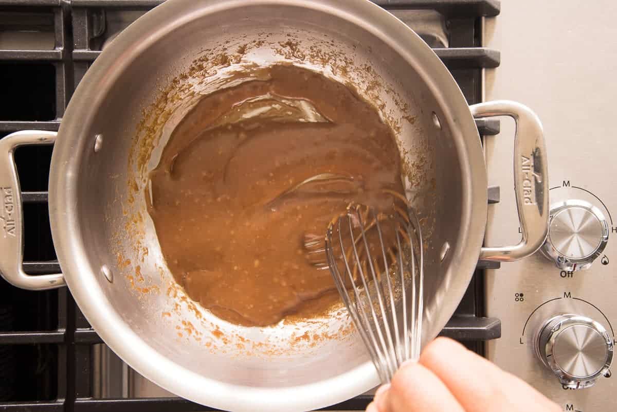 The Coquito toffee sauce caramel is thickened in a silver pot and stirred with a whisk