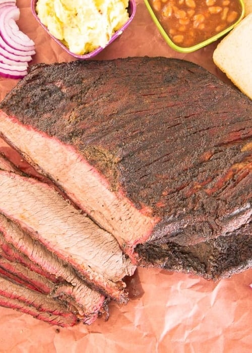 The sliced coffee-rubbed smoked brisket overhead shot surrounded by condiments and sides