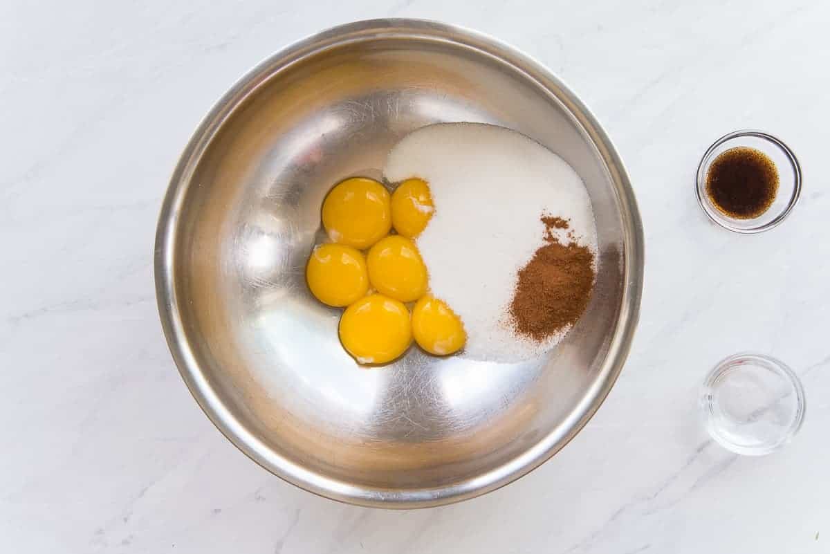 Egg yolks, sugar, and cinnamon in a silver mixing bowl.