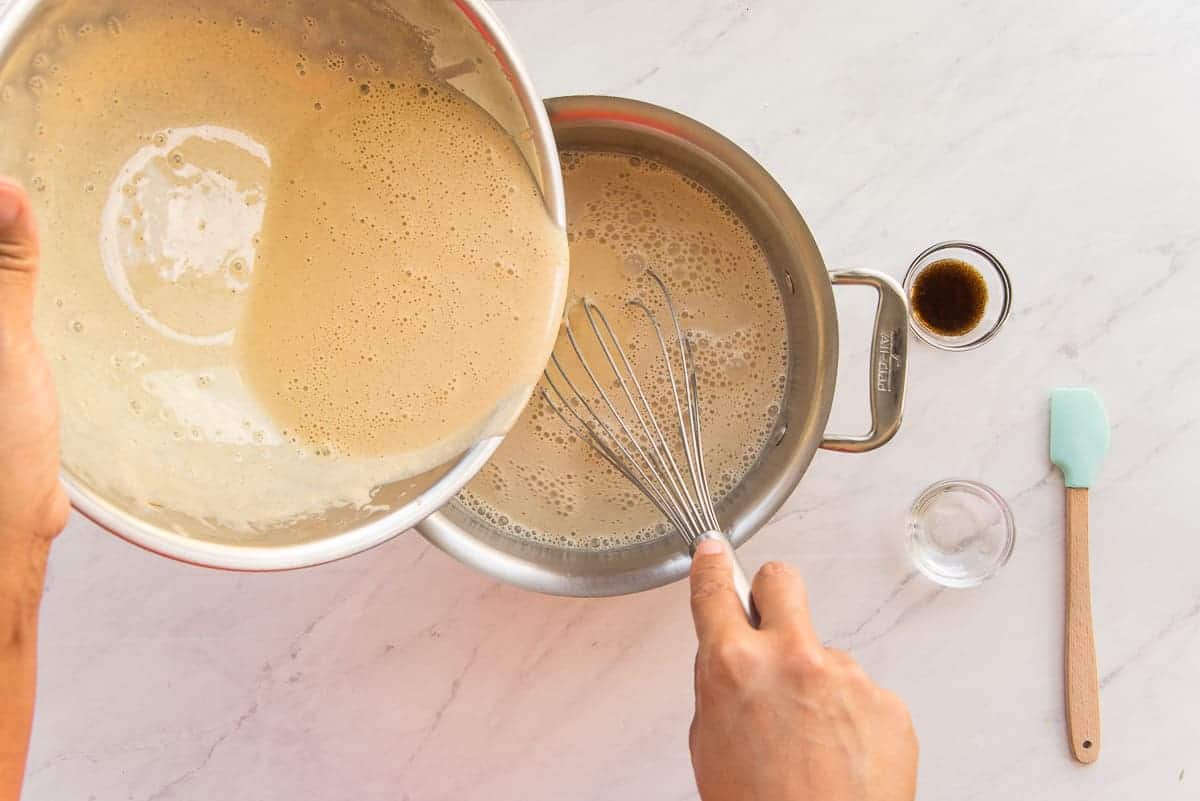 The tempered eggs are poured back into the hot coquito mixture in a silver pot.