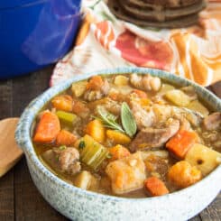 Horizontal image of a blue speckled bowl of Harvest Pork Stew next to a wooden soup spoon