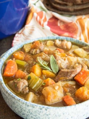 Horizontal image of a blue speckled bowl of Harvest Pork Stew next to a wooden soup spoon