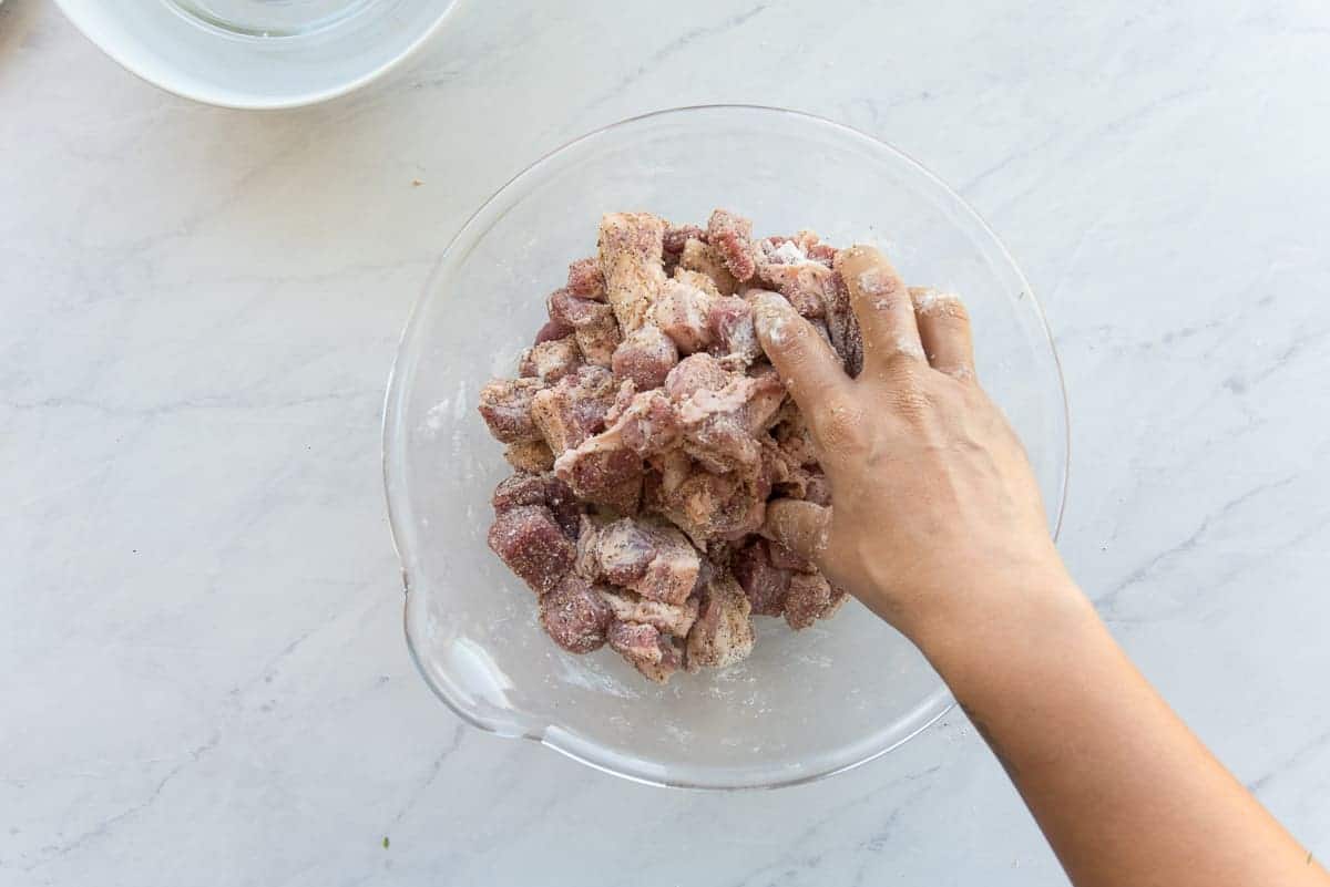 A hand tosses the meat in all-purpose flour to coat it.
