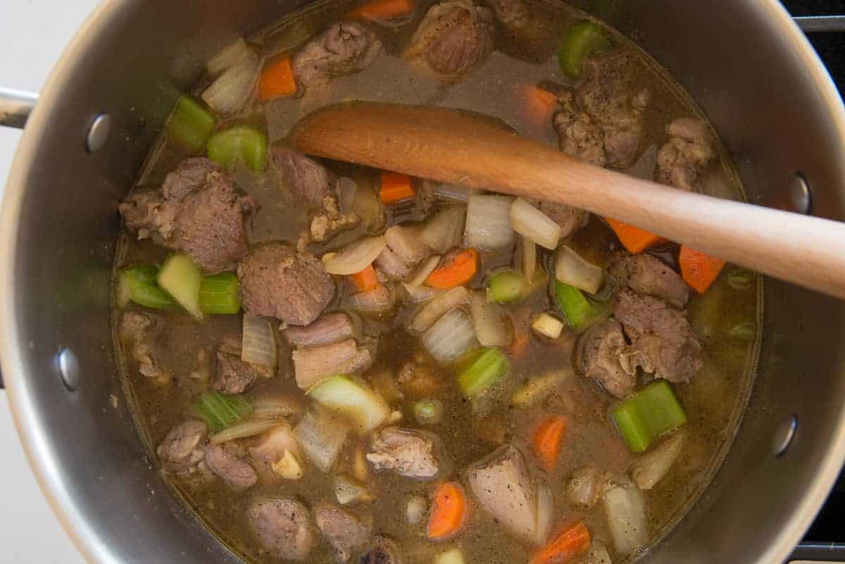 wooden spoon stirs the beef broth into the ingredients in the pot