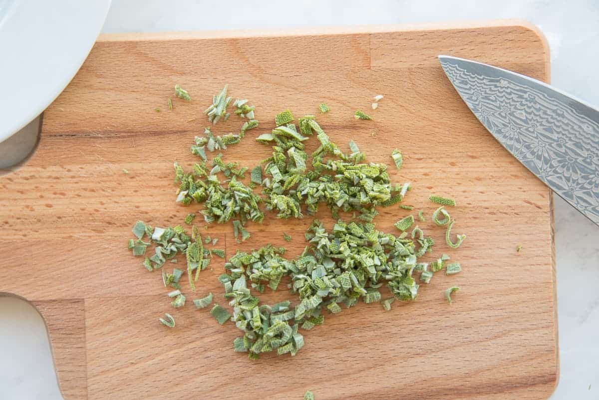 Sage is chopped on a wooden cutting board.