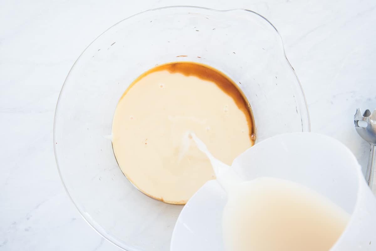 The sesame seed milk is poured into a glass mixing bowl of sweetened condensed milk and vanilla.