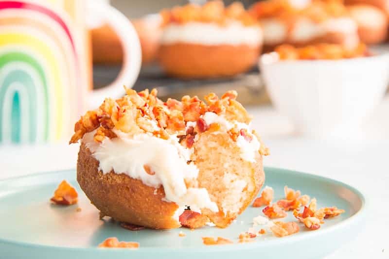 A maple bacon donut with a bite removed sits on a teal plate
