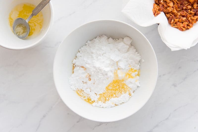 Melted butter added to a white bowl with powdered sugar and syrup.