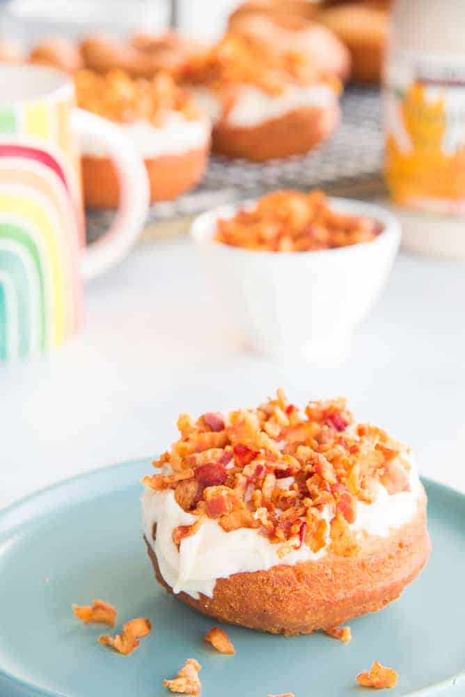 Lead image of a Maple Bacon Cake Donut on a teal plate. More donuts in the background 