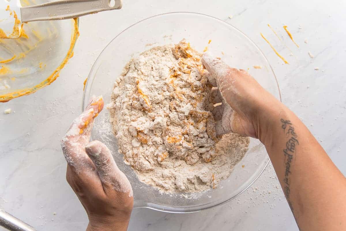 Two hands combine the pumpkin mixture in the flour and butter mixture.