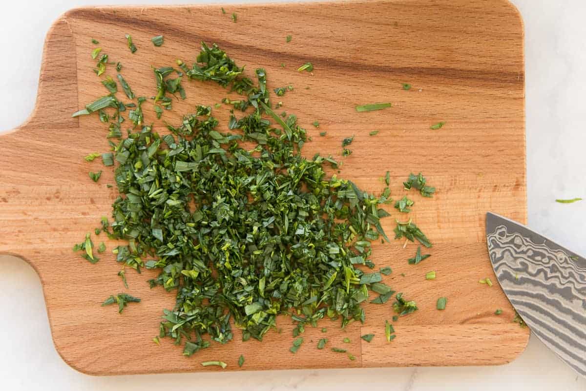 Fresh tarragon is chopped on a light-colored wooden board.