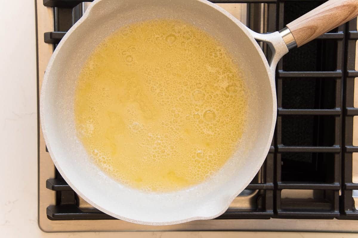 Butter has finished melting in a grey pot on a stove