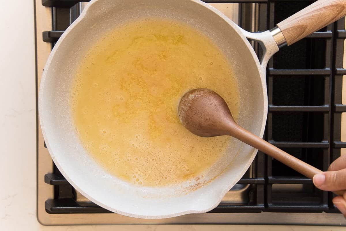 The melted butter is stirred with a dark wooden spoon in a grey pot
