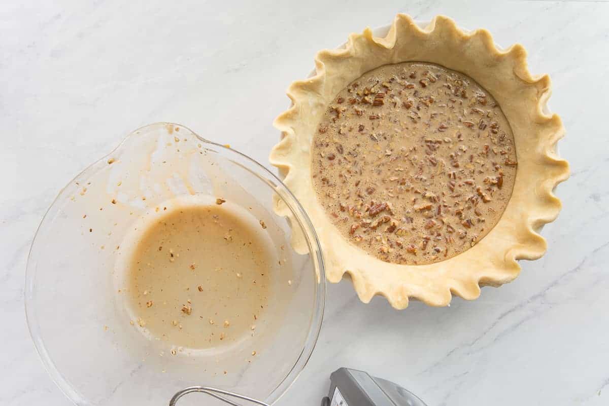 The chopped nut mixture is poured from a clear mixing bowl into the pie shell