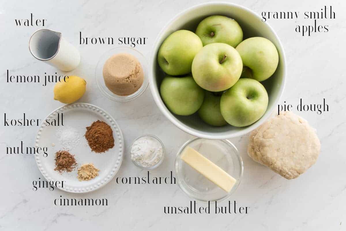 The ingredients to make Apple Cinnamon Pie: water, brown sugar, granny smith apples, pie dough, unsalted butter, cornstarch, cinnamon, ginger, nutmeg, kosher salt, and lemon juice.
