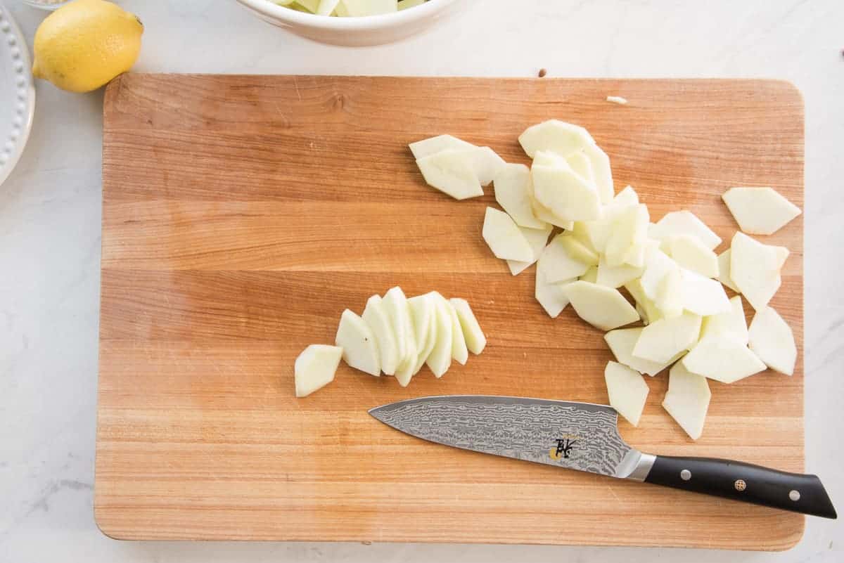 A knife on a brown wood cutting board after slicing apple wedges.