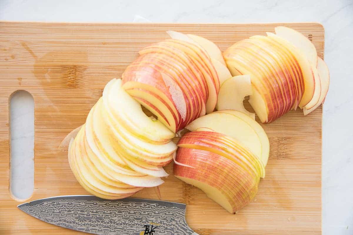 Thinly sliced honey crisp apples on a wooden cutting board.
