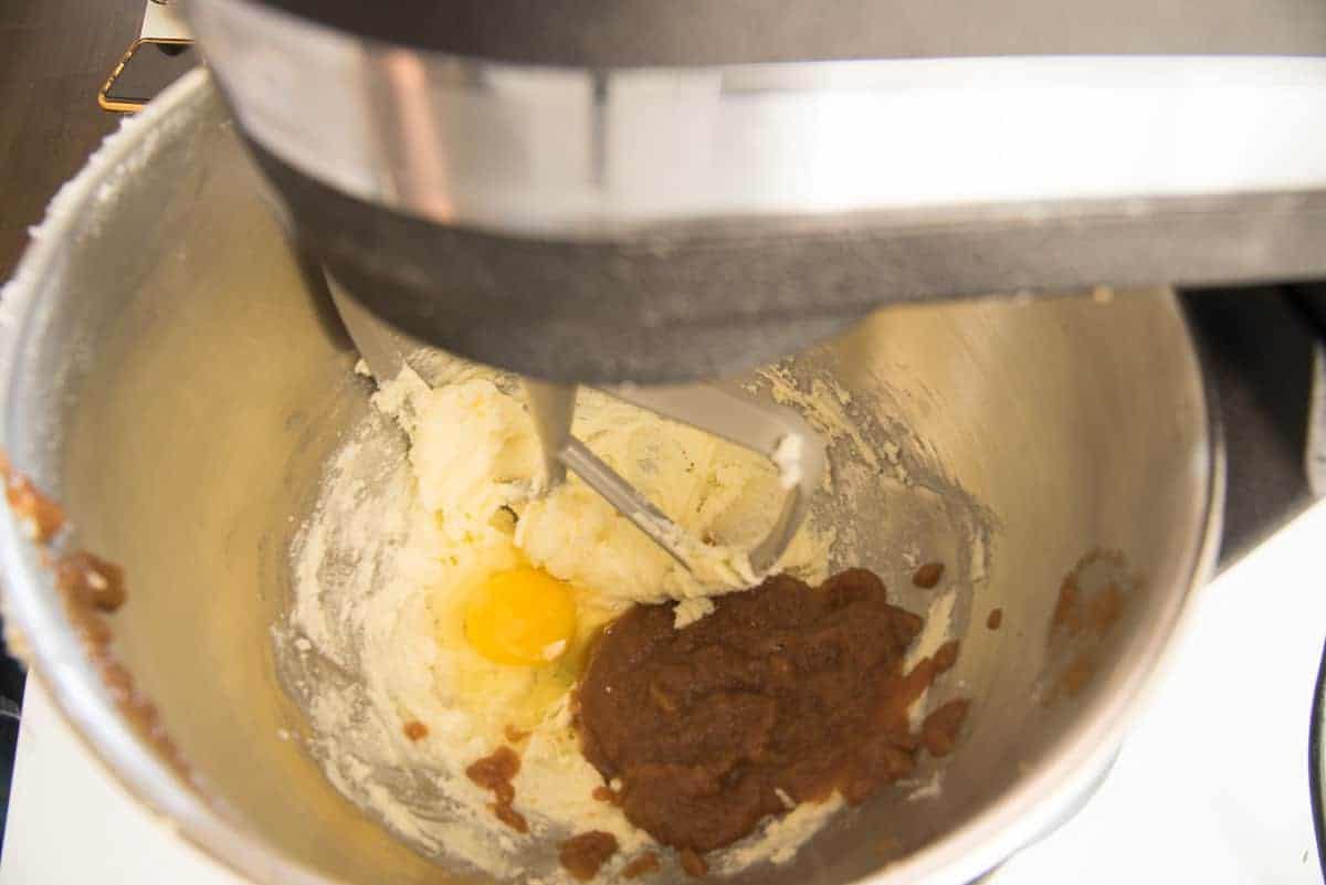 The egg and apple butter are added to the butter and sugar mixture in a silver mixing bowl.