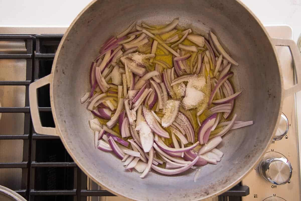 The onions and salt are added to the caldero of warm oil.