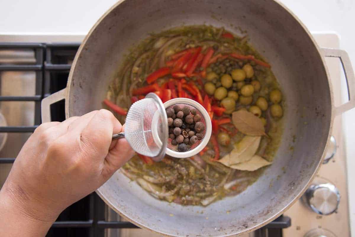 The allspice and peppercorns are added to a tea strainer before being added to the caldero of escabeche sauce.