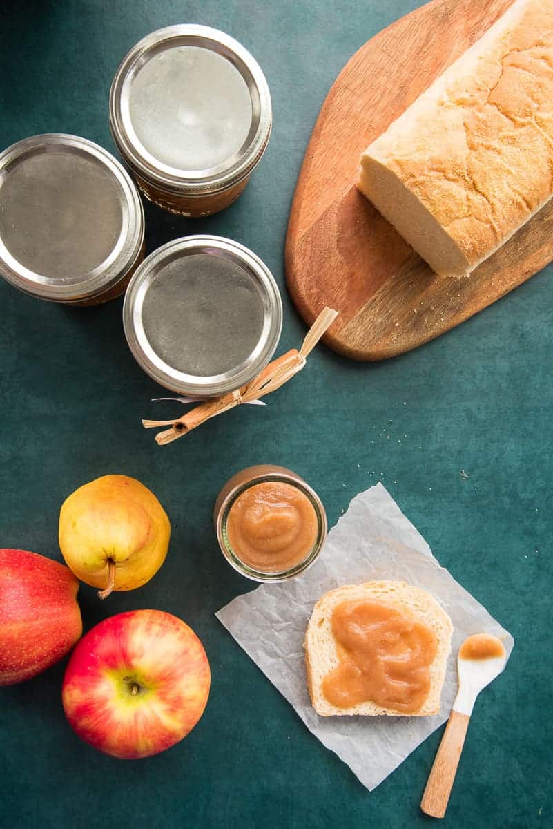 Overhead portrait image of three silver capped jars of Slow Cooker Apple Pear Butter next to an open jar and a slice of bread spread with the butter.