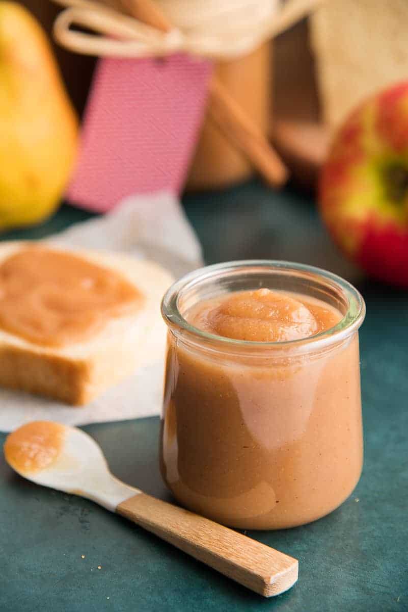 Portrait image of a glass jar of Slow Cooker Apple Pear Butter next to a mother of pearl spoon.