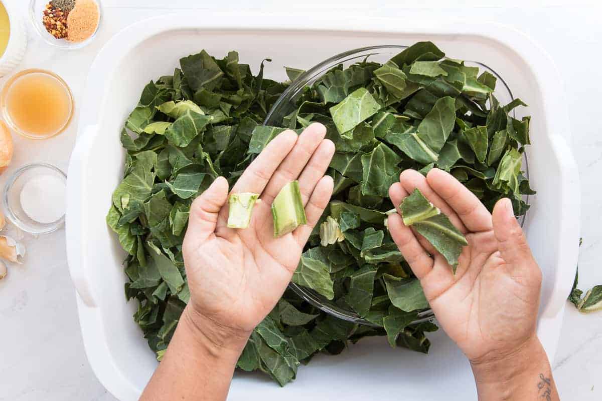 Two hands display what to get rid of and what is okay to keep from the collard greens.