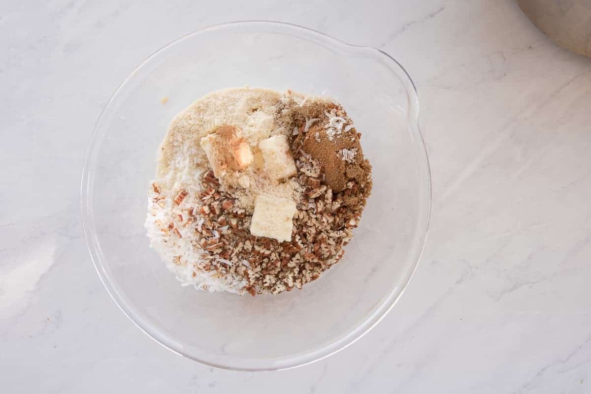 The ingredients to make the coconut pecan topping are added to a clear glass mixing bowl.