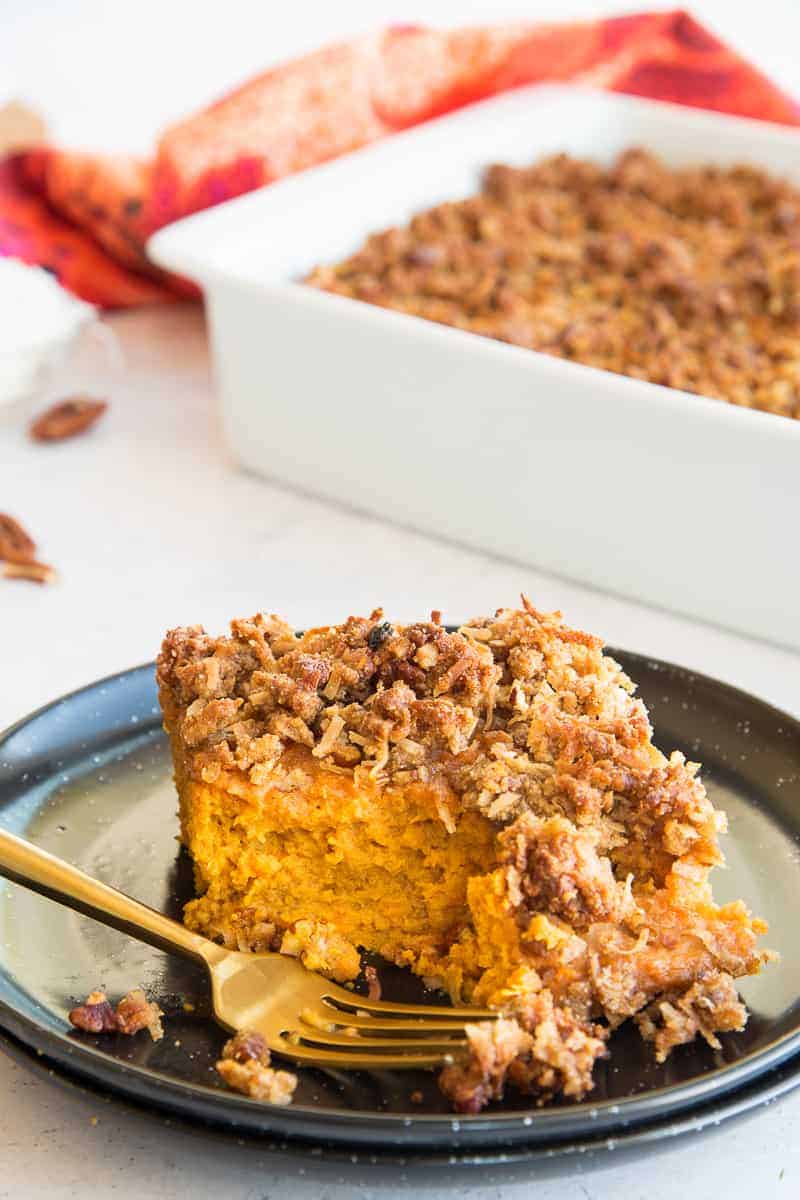 Lead image of a serving of sweet potato casserole with coconut pecan topping with a bite removed from a gold fork that sits in front of the serving on the plate.