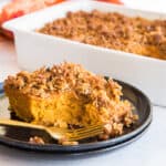 Preview image of sweet potato casserole with coconut pecan topping on a black plate with white specks in front is a gold fork.