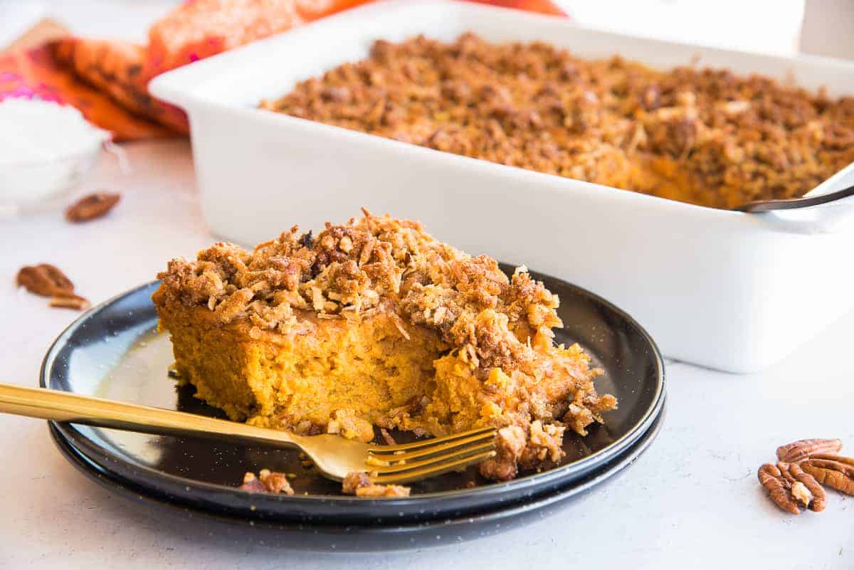 Preview image of sweet potato casserole with coconut pecan topping on a black plate with white specks in front is a gold fork.