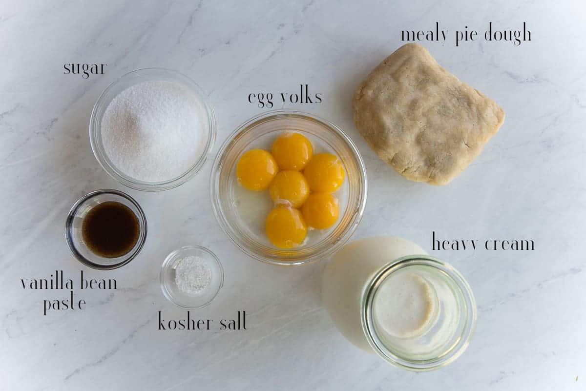The ingredients to make the recipe: sugar, egg yolks, mealy pie dough, heavy cream, kosher salt, and vanilla bean paste.