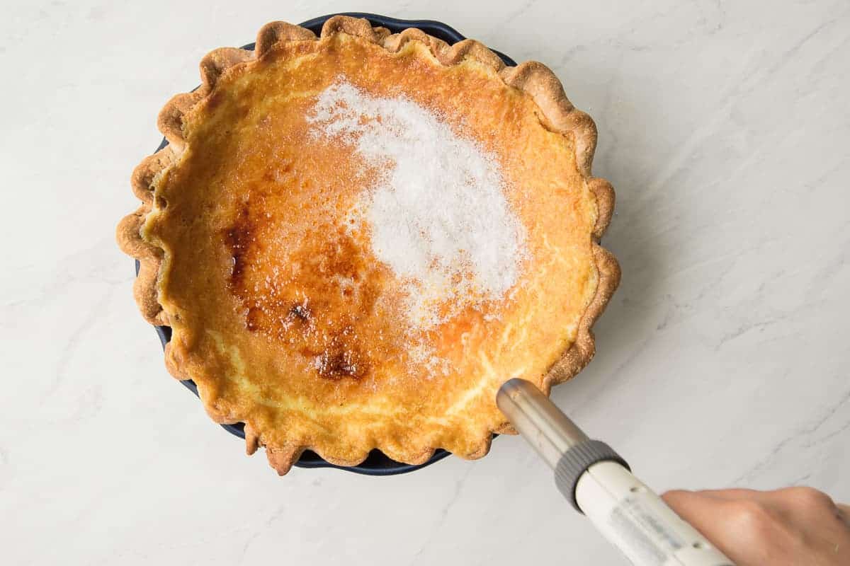 A hand uses a butane torch to melt the sugar on the Crème Brûlée Pie