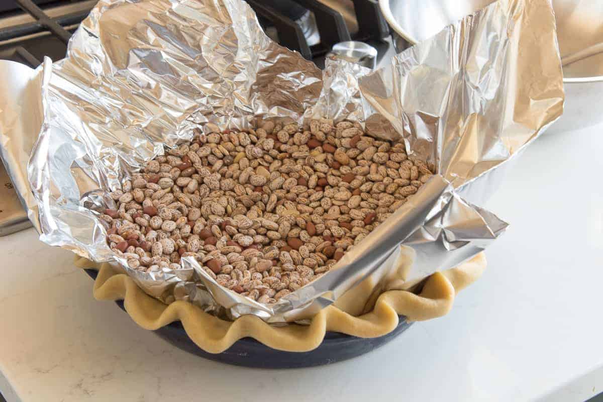 Dried beans fill a sheet of aluminum foil set inside of a pie shell before it is blind baked.
