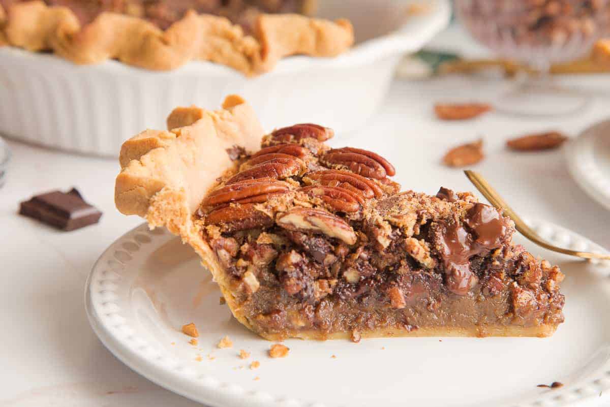 Close-up horizontal image of side of a slice of Maple Bourbon Pecan Pie with Chocolate Chunks on a white beaded plate.