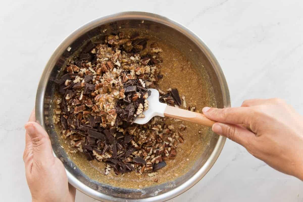 The chocolate and nuts are folded into the sugar and egg mixture in a silver mixing bowl.