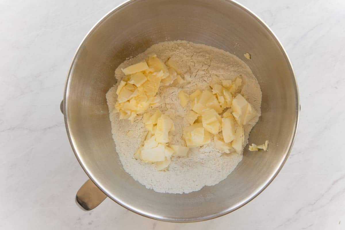 Sliced butter is added to the dry ingredients in the bowl of a stand mixer