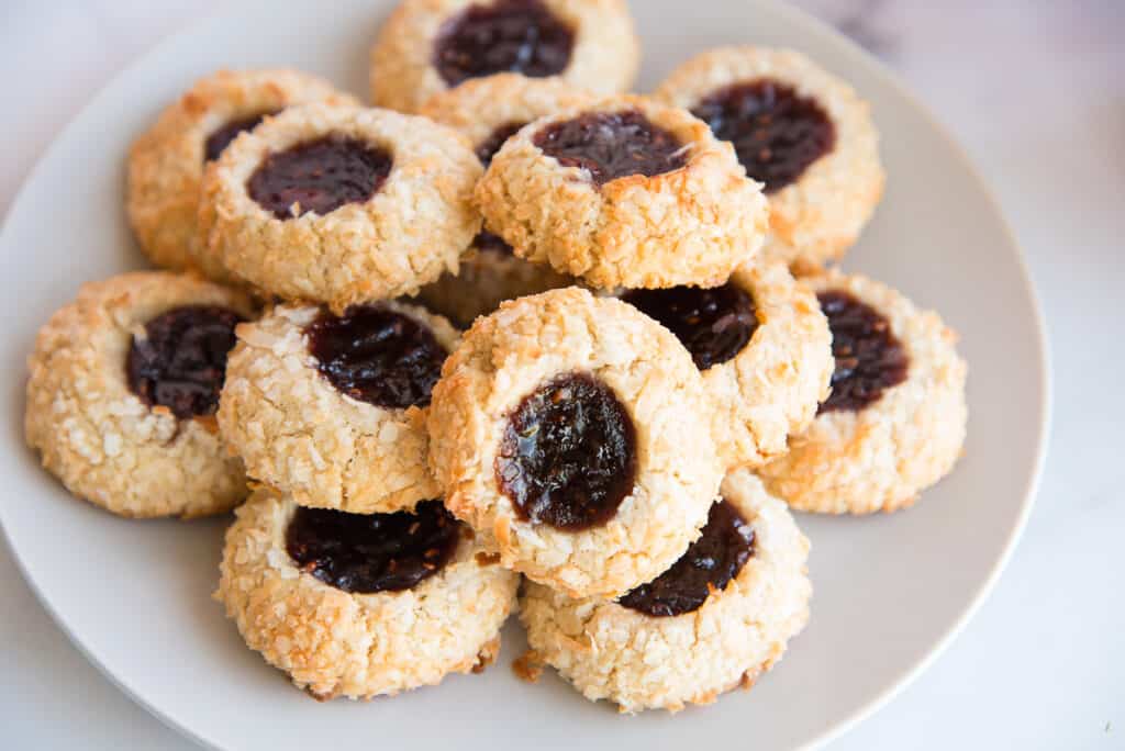 Horizontal close up of a light grey plate of Coconut Raspberry Thumbprint Cookies