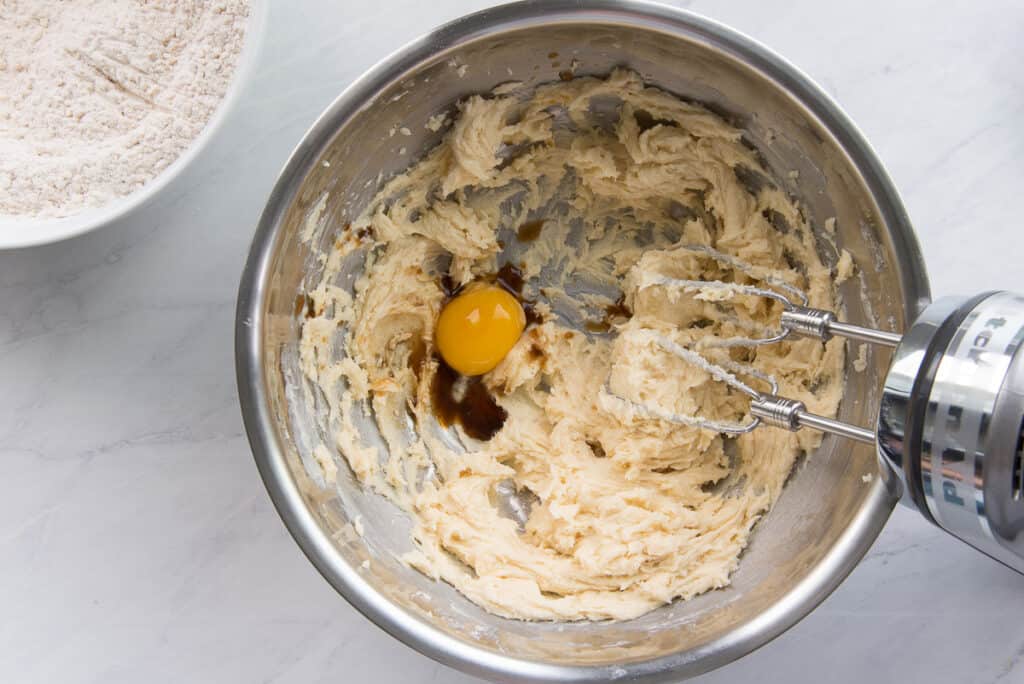 The egg yolk and vanilla are added to the butter sugar mixture in the bowl.